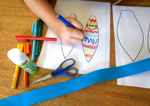 Boy using coloured textas to decorate paper bunny ear template.