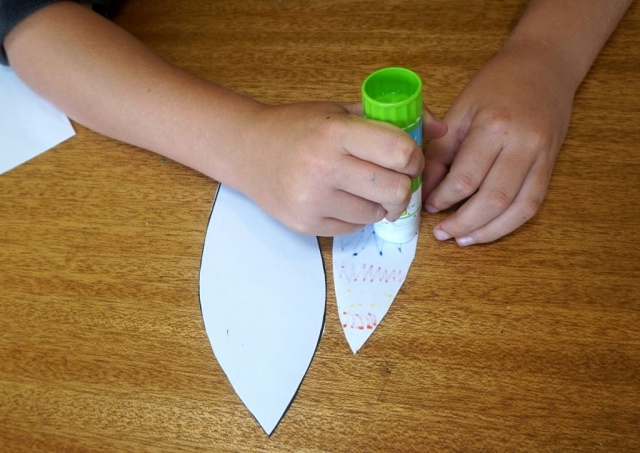 Boy using glue stick to apply glue to the back of the inner ear part of the paper template.