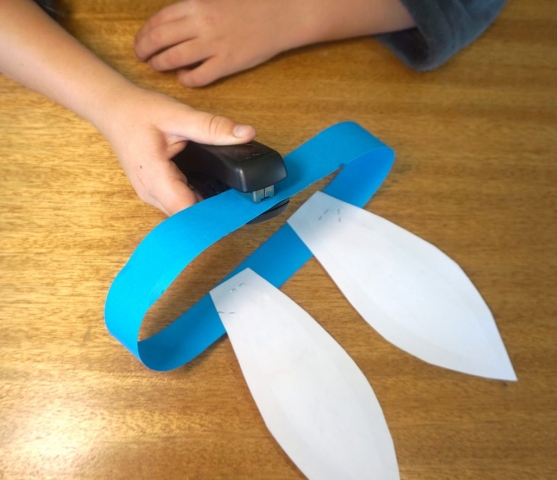 Boy stapling paper ribbon ends together to form a circle.