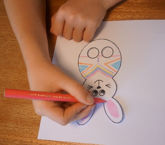 Boy using coloured textas to decorate paper bunny finger puppet template.