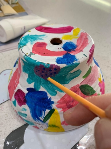 A white garden pot with colourful paint splotches.