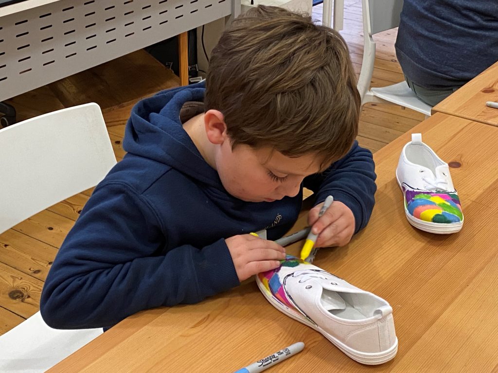 A boy painting canvas shoes with colourful sharpie markers