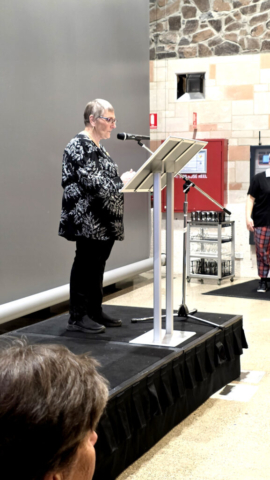 Margaret Carter, President of the South East Art Society A woman with grey hair wearing a black and white jumper standing at a podium on a stage